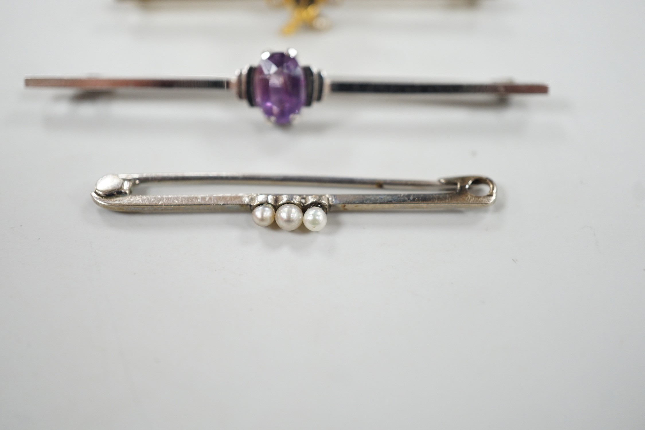 A 9ct white gold and synthetic? sapphire set bar brooch, 45mm and three other bar brooches including yellow metal and seed pearl, white metal and seed pearl and a 9ct and amethyst bar brooch, gross weight 8.1 grams.